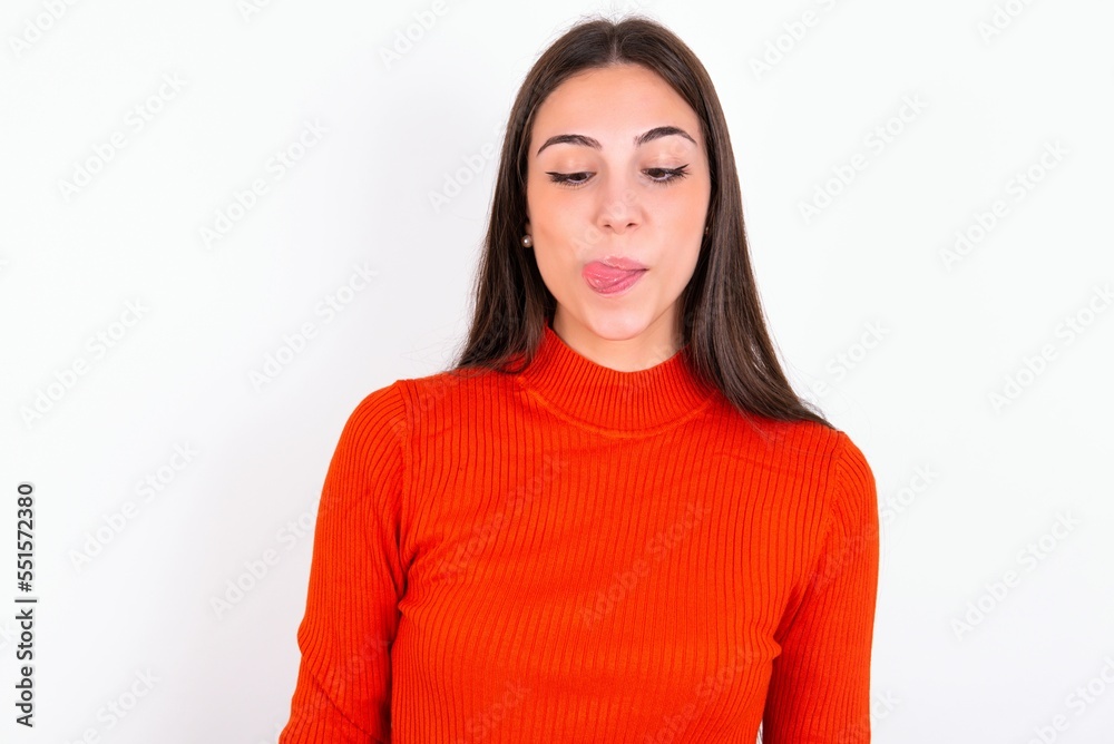 Funny Young caucasian woman wearing red sweater over white background makes grimace and crosses eyes plays fool has fun alone sticks out tongue. Funny Young caucasian woman wearing red sweater over white background makes grimace and crosses eyes plays fool has fun alone sticks out tongue.