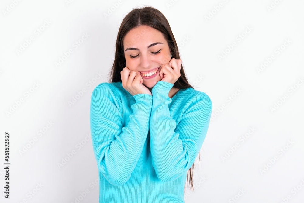 Young caucasian woman wearing blue sweater over white background grins joyfully, imagines something pleasant, copy space. Pleasant emotions concept. Young caucasian woman wearing blue sweater over white background grins joyfully, imagines something pleasant, copy space. Pleasant emotions concept.