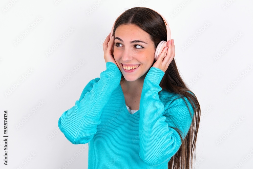 Young caucasian woman wearing blue sweater over white background wears stereo headphones listens music concentrated aside. People hobby lifestyle concept Young caucasian woman wearing blue sweater over white background wears stereo headphones listens music concentrated aside. People hobby lifestyle concept