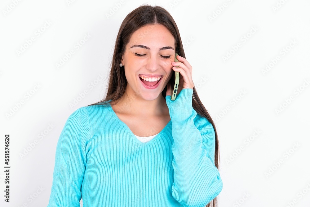 Overemotive happy Young caucasian woman wearing blue sweater over white background laughs out positively hears funny story from friend during telephone conversation Overemotive happy Young caucasian woman wearing blue sweater over white background laughs out positively hears funny story from friend during telephone conversation