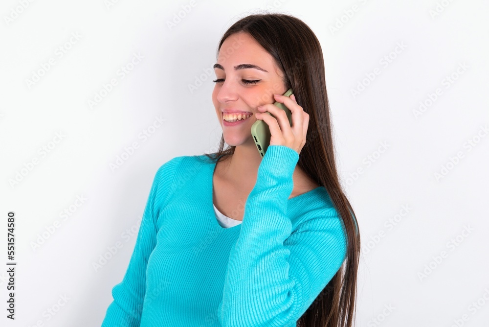 Happy joyful charming Young caucasian woman wearing blue sweater over white background talk speak phone smile good mood Happy joyful charming Young caucasian woman wearing blue sweater over white background talk speak phone smile good mood