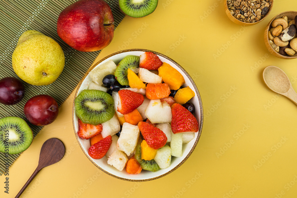 Fresh fruit salad in a bowl. Multicolored and tropical fruits. Pineapple, mango, grape, strawberry, papaya, melon, kiwi. Additional with chestnuts and granola. Top view. Selective focus