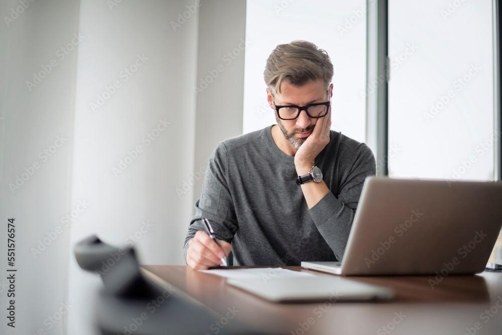 Mddle aged businessman looking thoughtfully while using laptop and working at the office Mddle aged businessman looking thoughtfully while using laptop and working at the office