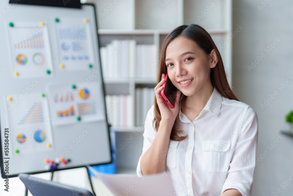 Attractive and attractive young Asian businesswoman is using phone to talk to customers and using laptop for work happily. Attractive and attractive young Asian businesswoman is using phone to talk to customers and using laptop for work happily.