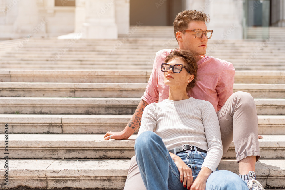 Young beautiful hipster couple in sunglasses in love sitting stairs on old city street