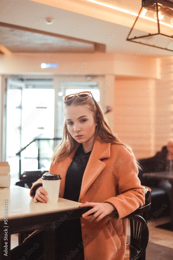 beautiful young woman with a cup of takeaway coffee and donuts sits in a cafe