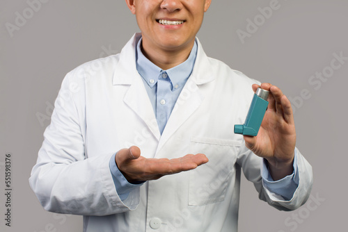 Cheerful middle aged korean male therapist in white coat show inhaler for breathing, emergency help