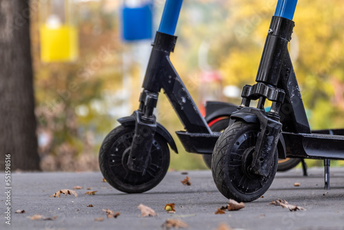 Electric Scooters wheels close-up on asphalt road in autumn park with colorful blurred cableway background. E-scooter parking in city recreation park