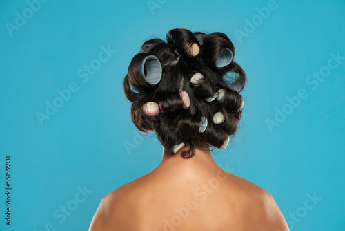 Фотография Back view of a young woman with hair curlers posing on a blue studio background