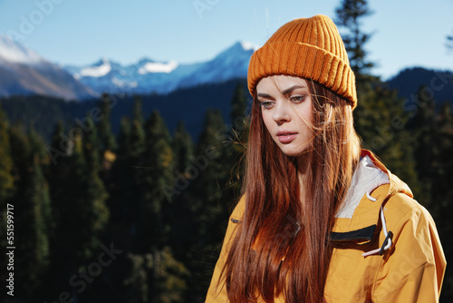 Young woman hiker portrait in yellow raincoat looking into camera and smiling traveling and hiking in the mountains in the sunset sun freedom