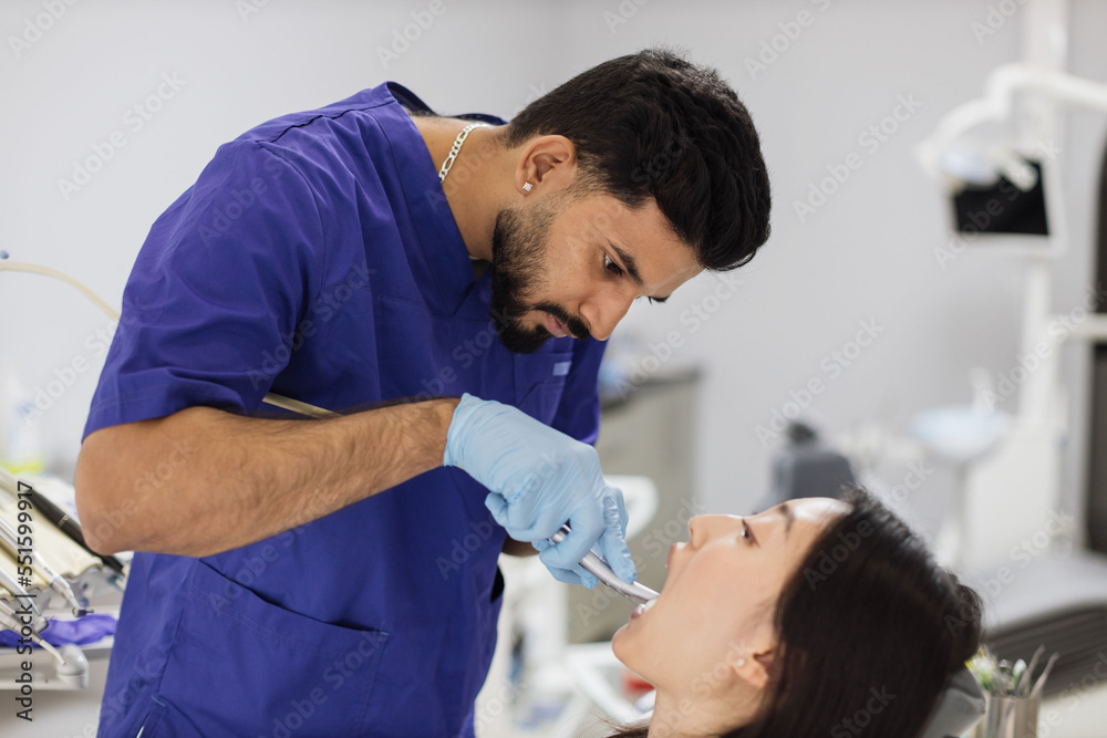 Fototapeta premium Happy patient and dentist concept. Young bearded asian male stomatologist treating teeth of a beautiful asian woman patient, using tooth drill. Oral health and hygiene.