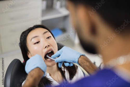 Happy patient and dentist concept. Young bearded asian male stomatologist treating teeth of a beautiful asian woman patient  using tooth drill. Oral health and hygiene.