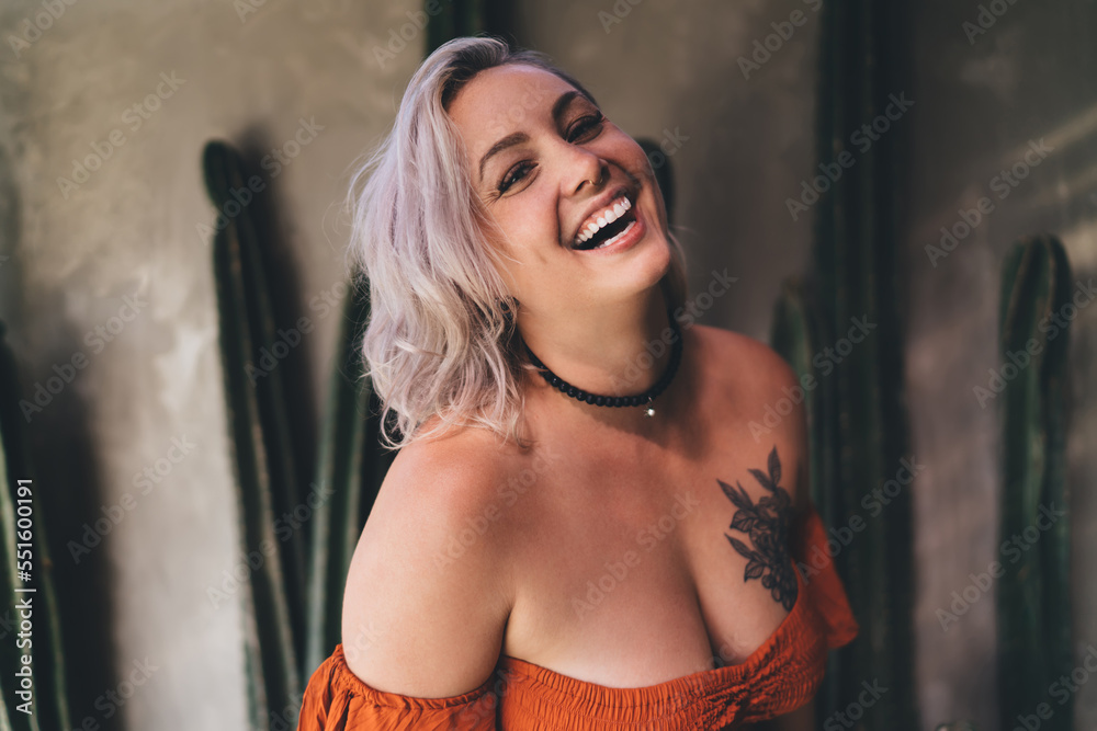 Fototapeta premium Cheerful woman with tattoo on chest standing in cafe