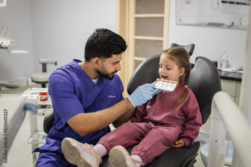 Tooth teeth tone palette. Stomatologist orthodontist male dentist choosing selecting color of patient cute little preschool girl teeth for whitening at clinic. Tooth teeth tone palette. Stomatologist orthodontist male dentist choosing selecting color of patient cute little preschool girl teeth for whitening at clinic.