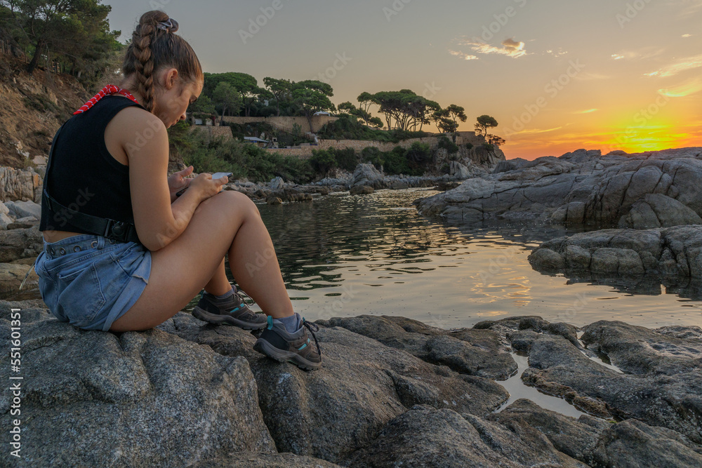 Girl looking at her mobile while sunrise on a beach in Catalonia in Spain