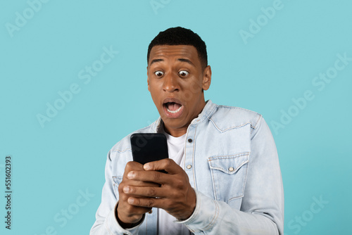 Scared shocked funny young african american guy in casual with open mouth scream, look, at phone © Prostock-studio