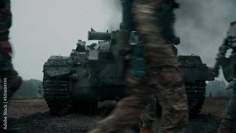 Ukrainian soldiers on a pixel and multicam uniform walk behind a T-72 tank on the battlefield