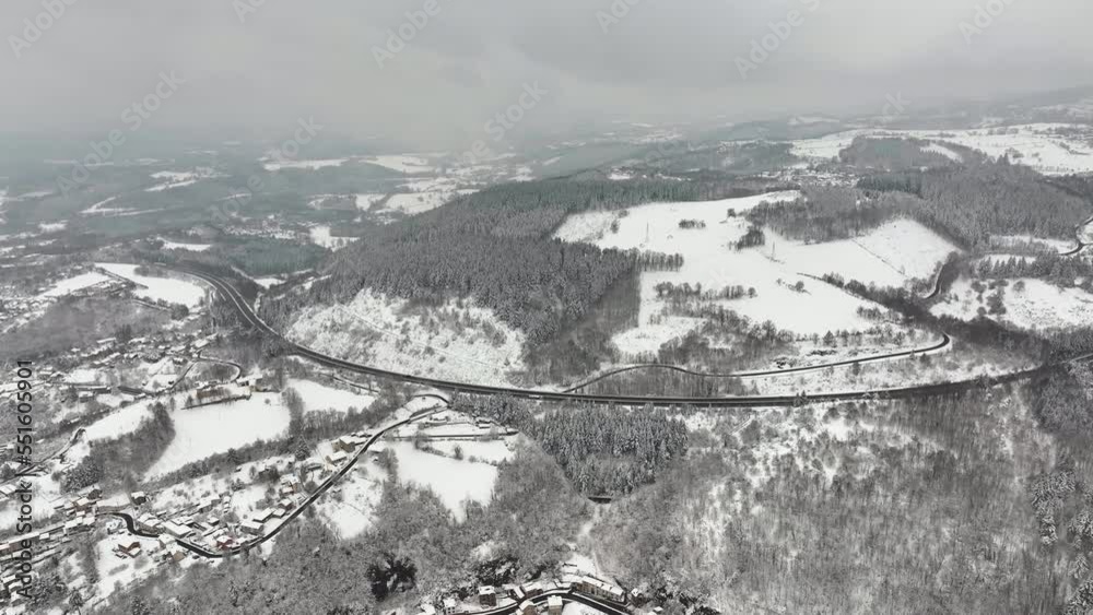 Aerial foggy landscape with mountain road covered with fresh fallen snow during heavy snowfall in winter mountain forest on cold quiet day Aerial foggy landscape with mountain road covered with fresh fallen snow during heavy snowfall in winter mountain forest on cold quiet day