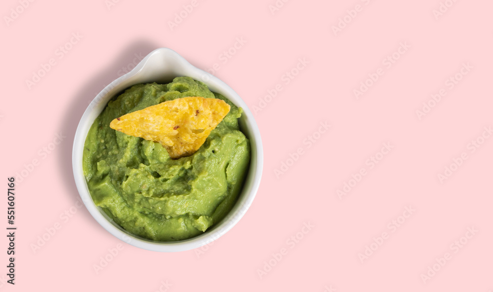 top view of a bowl with guacamole and nachos on a pink background with copy space