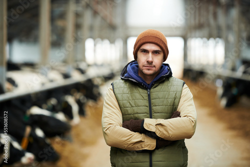 Young serious male owner of large modern livestock farm in waistcoat and beanie cap crossing arms on chest while looking at camera photo