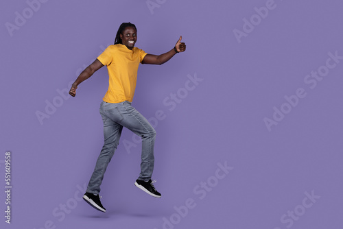 Excited african guy running in the air, showing thumb up © Prostock-studio