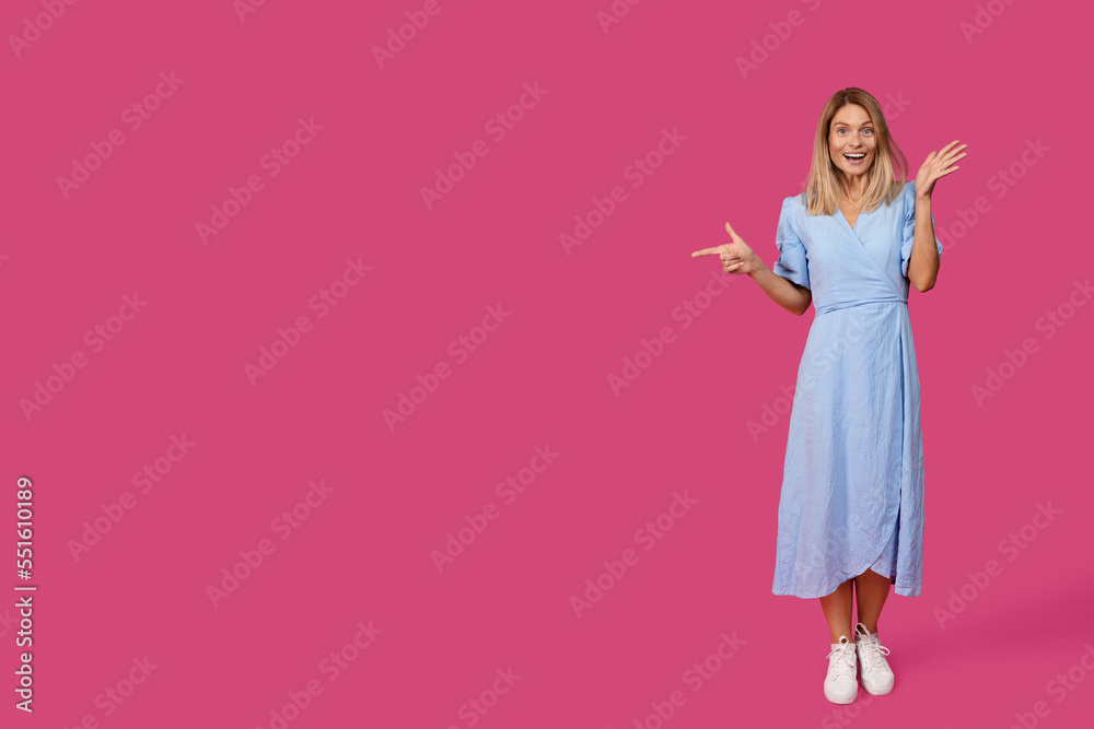 Cheerful shocked middle aged caucasian female blonde in dress pointing finger at empty space Cheerful shocked middle aged caucasian female blonde in dress pointing finger at empty space