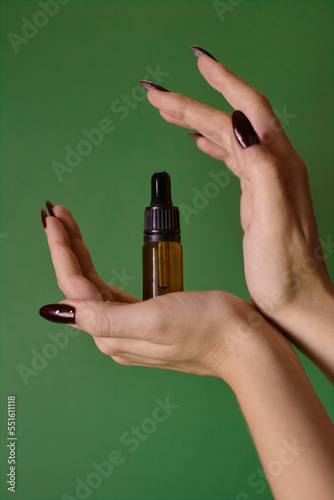 Glass bottle with a pipette in hands on a green background. Essential oils. Women s cosmetics on a bright background.
