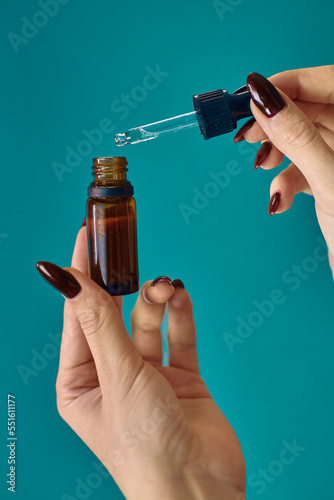 The girl drips oil with a pipette. Glass bottle of essential oils in hands. Women's cosmetics on a blue background.