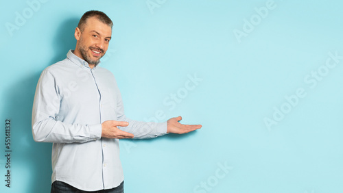 Happy handsome middle aged man in casual showing free space and advertising something on blue studio background
