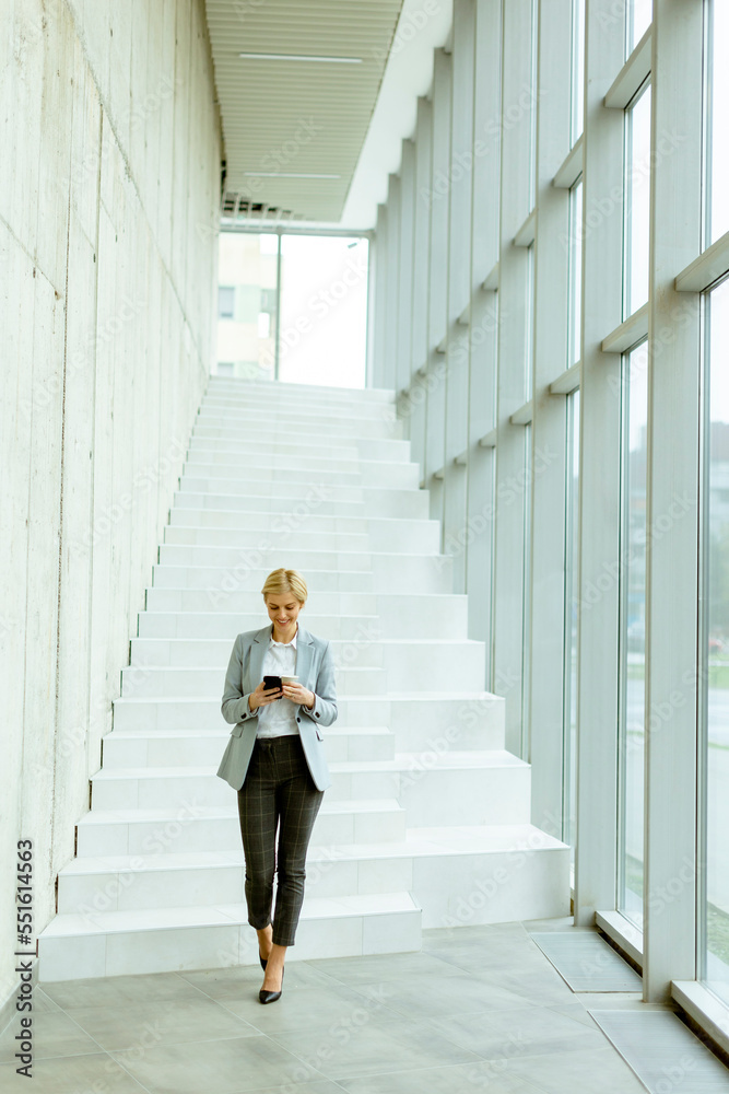 Businesswoman using mobile phone on modern office hallway