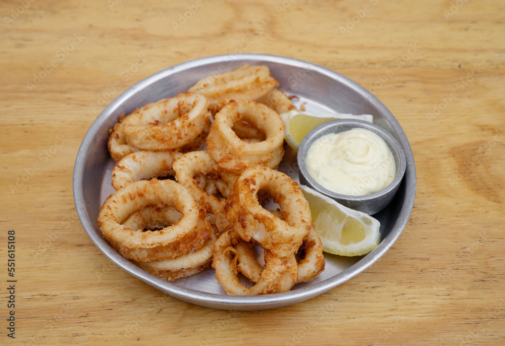 Seafood. Closeup view of fried squid rings with lemon and a dipping sauce in a metal dish on the wooden table.