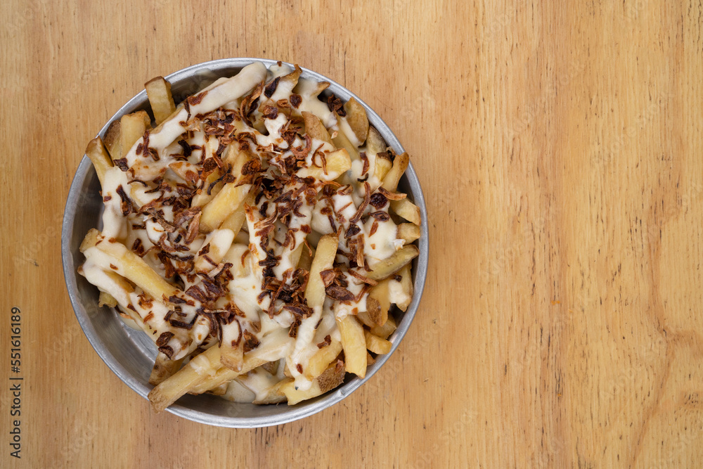 Fries. Top view of french fries with melted cheese and crispy onion, in a metal dish with a wooden background. Fries. Top view of french fries with melted cheese and crispy onion, in a metal dish with a wooden background.
