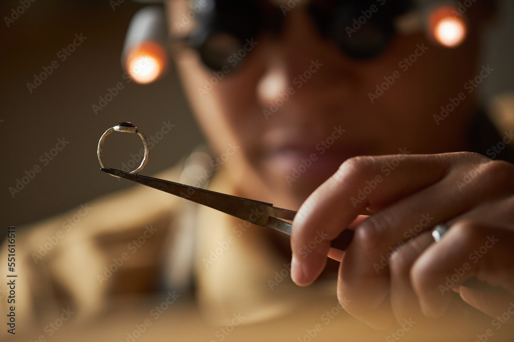 Macro shot of jeweler holding golden ring with tweezers in artisanal workshop
