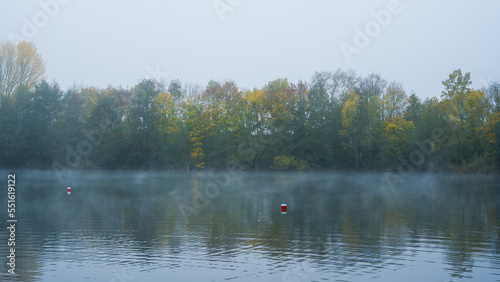 Fog over water surface of lake, foggy autumn trees in background