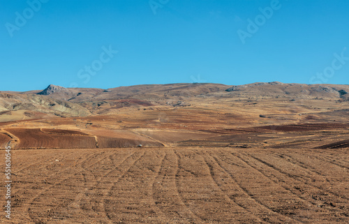 Empty field in front of mountainous terrain and the blue sky in a sunny day. Distant mountain hills in autumn with copy space.
