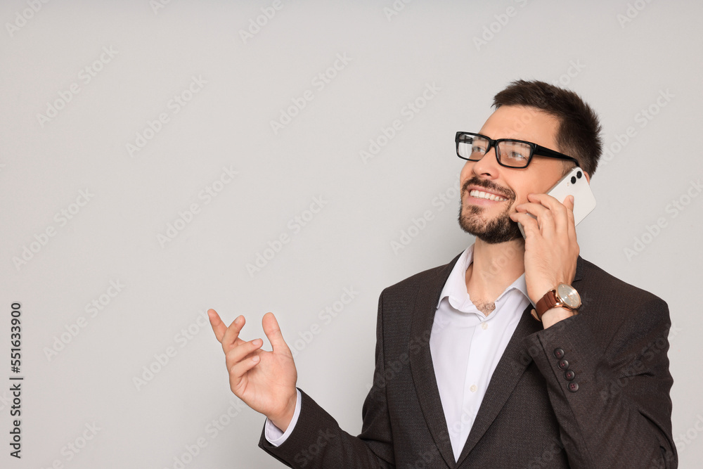 Handsome man in suit talking on smartphone against light grey background. Space for text Handsome man in suit talking on smartphone against light grey background. Space for text