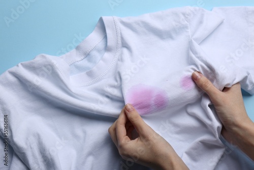 Woman holding white shirt with purple stains on light blue background, top view