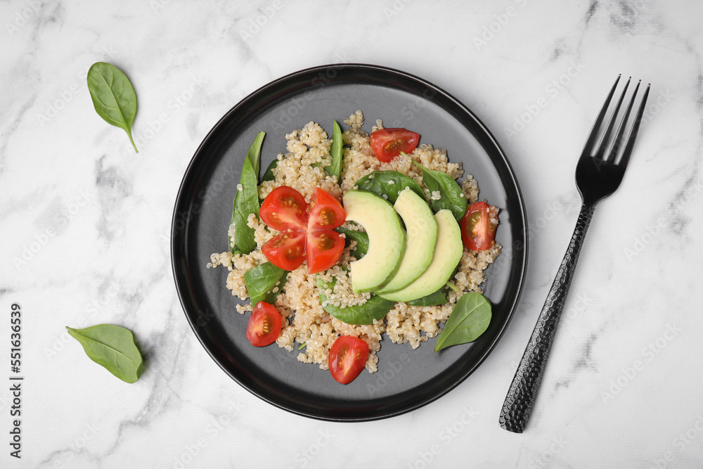 Delicious quinoa salad with tomatoes, avocado slices and spinach leaves served on white marble table, flat lay