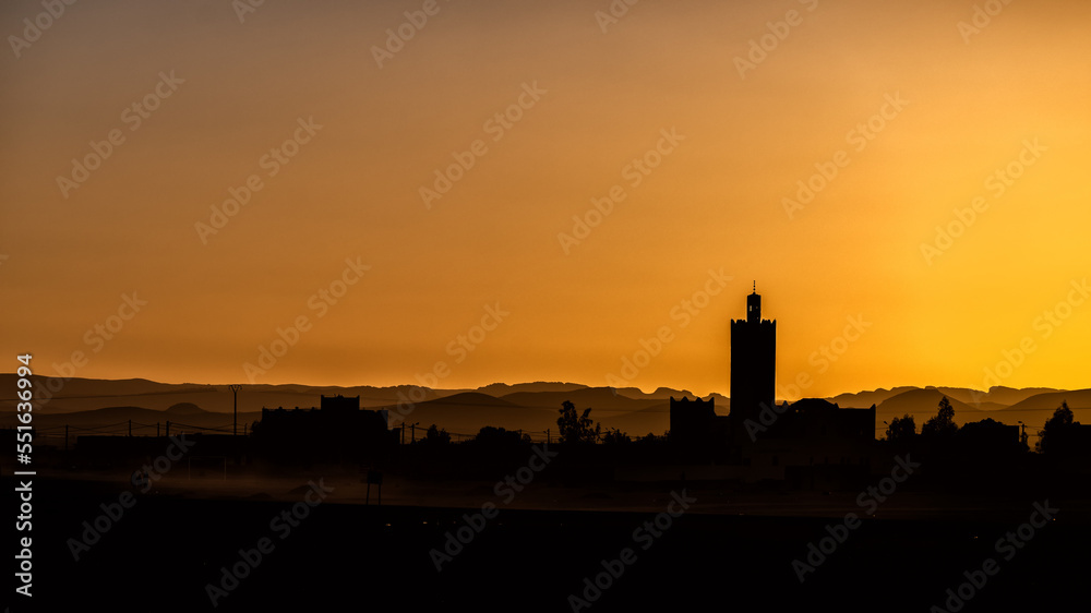 Silhouette of a typical Arab village with a mosque minaret at sunset. Ksar Tanamouste, Sahara, Morocco.