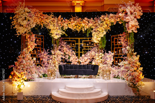 Front view of luxury armchair for newlyweds among floral compositions, placed on stand in restaurant on background of arch