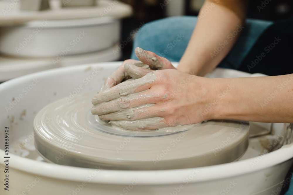 Closeup of potter hands working on pottery wheel in ceramic studio with clay hands side view with pottery wheel in motion