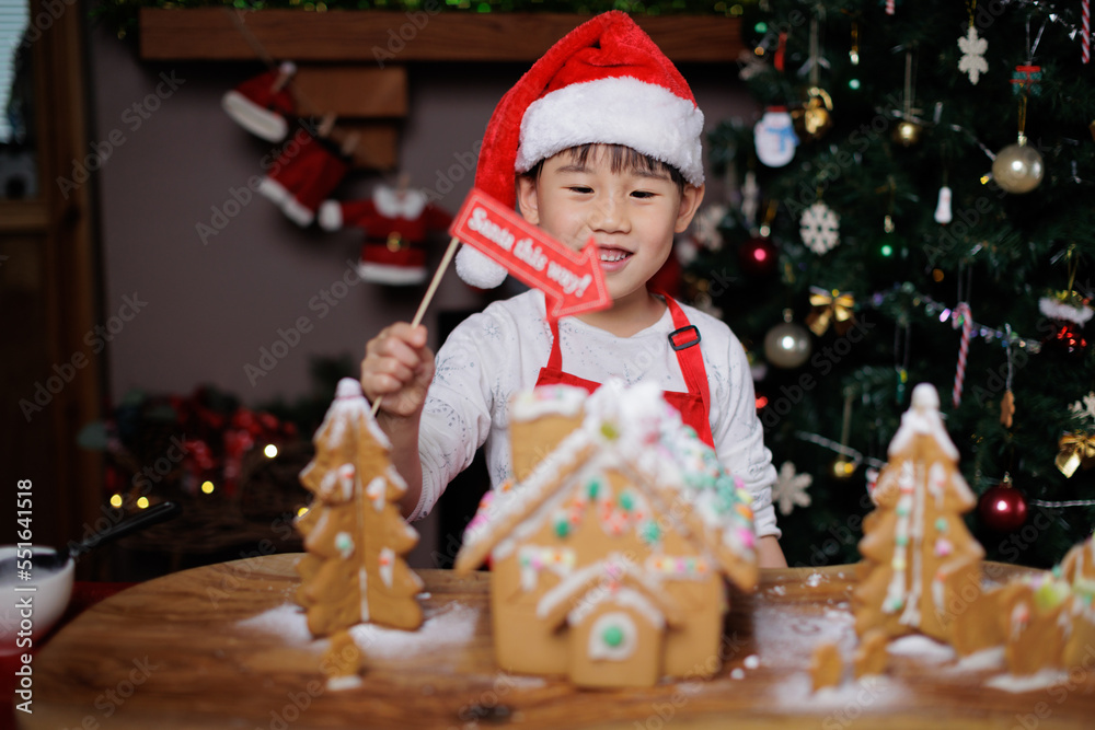 young girl wearing Santa hat was decorating gingerbread house for celebrating Christmas at home young girl wearing Santa hat was decorating gingerbread house for celebrating Christmas at home
