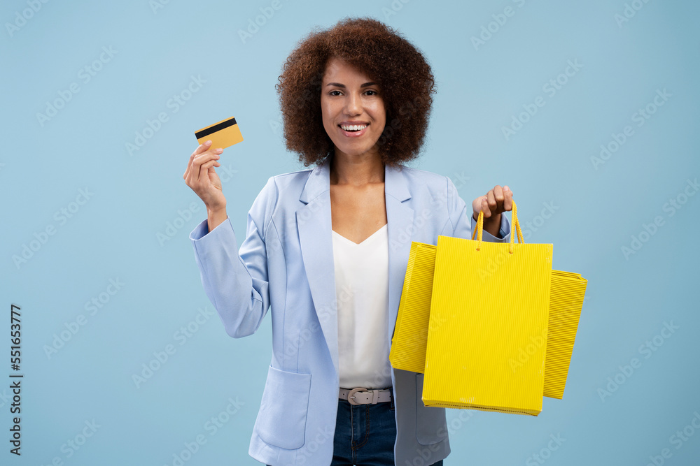 Smiling African American woman holding credit card and shopping bags isolated on blue background. Shopping, sales concept 