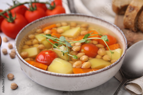 Tasty chickpea soup in bowl and ingredients served on white table, closeup