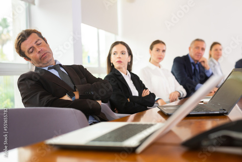 Tired middle aged mature white businessman in formal suit napping during corporate team meeting sitting at table in conference room