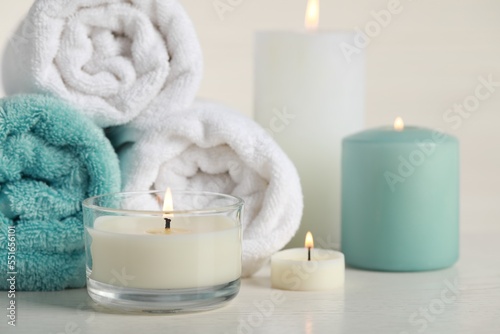 Beautiful spa composition with burning candles and rolled towels on white table, closeup