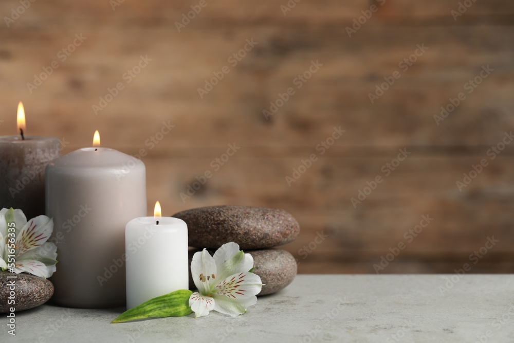 Beautiful composition with burning candles, spa stones and flowers on light grey table. Space for text Beautiful composition with burning candles, spa stones and flowers on light grey table. Space for text