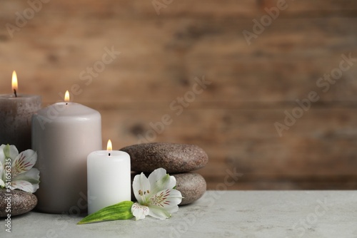 Beautiful composition with burning candles  spa stones and flowers on light grey table. Space for text