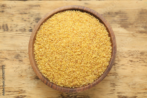 Bowl of uncooked bulgur on wooden table, top view