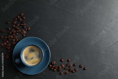 Cup of aromatic coffee and beans on black table, top view. Space for text